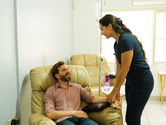 Cheerful nurse and patient smiling looking happy while getting IV drip therapy and vitamin minerals cocktail for a system detox